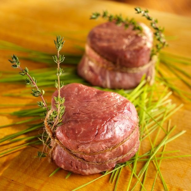 Juicy, medium-rare steak being sliced on a wooden cutting board, showcasing its tender pink interior and seared crust, with a carving knife and fork positioned for serving.